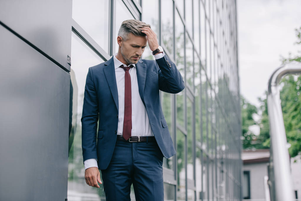 вибірковий фокус засмученого бізнесмена в офіційному одязі, що стоїть біля будівлі і торкається волосся
  - Фото, зображення