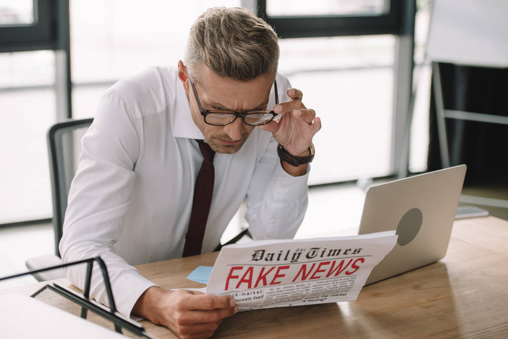 foco seletivo do empresário tocando óculos enquanto lê jornal com notícias falsas
  - Foto, Imagem