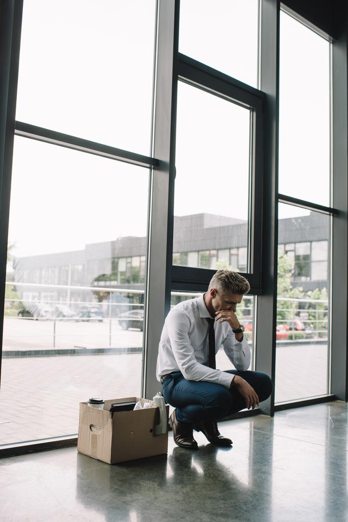 hombre de negocios despedido cubriendo la boca mientras estaba sentado caja de cartón en la oficina
  - Foto, Imagen