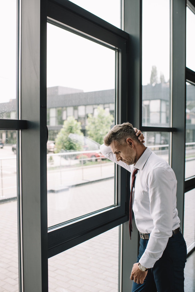 расстроенный бизнесмен в костюме, стоящий возле окон в офисе
  - Фото, изображение