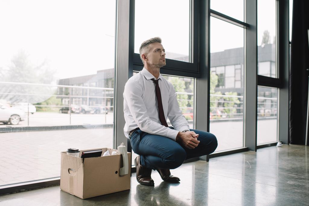 upset and fired man in suit sitting near carton box  - Photo, Image