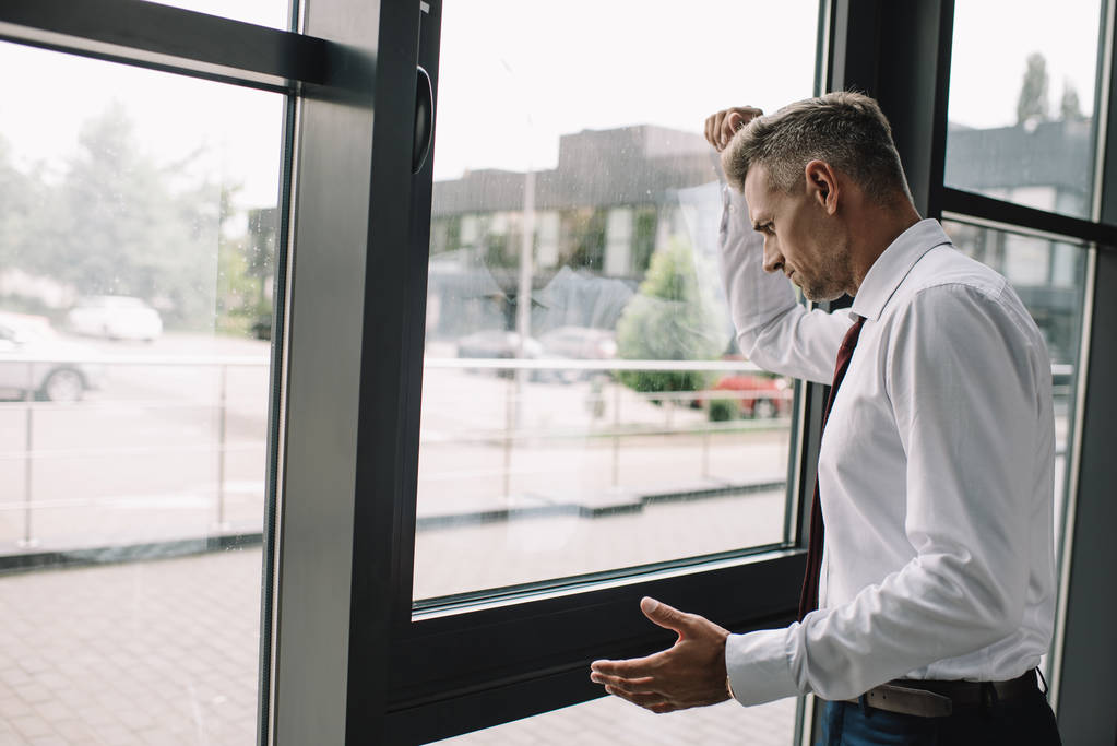 αναστατωμένος επιχειρηματίας στέκεται με σφικτά γροθιά κοντά στα παράθυρα - Φωτογραφία, εικόνα