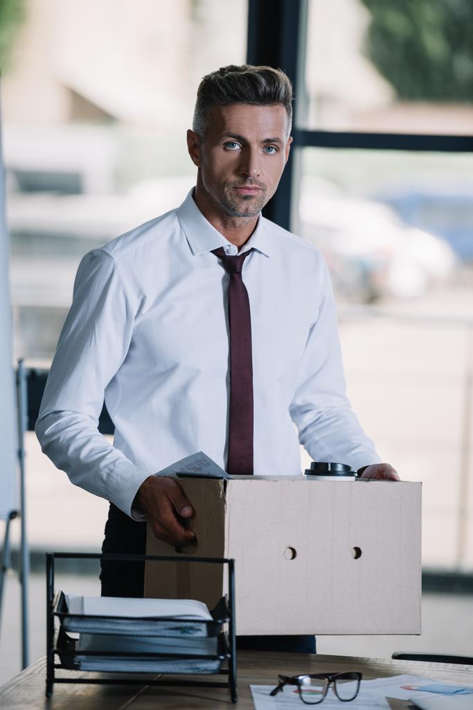 licencié homme d'affaires tenant boîte tout en se tenant près du lieu de travail et en regardant la caméra
  - Photo, image
