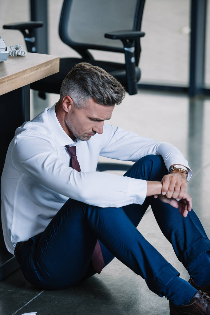 homem de negócios chateado sentado no chão perto do local de trabalho no escritório
  - Foto, Imagem