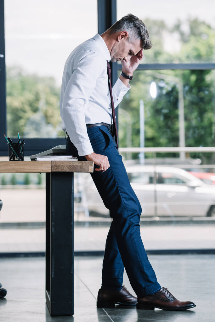 üzgün adam ahşap masa nın yanında duran ve ofiste kafa dokunmadan  - Fotoğraf, Görsel
