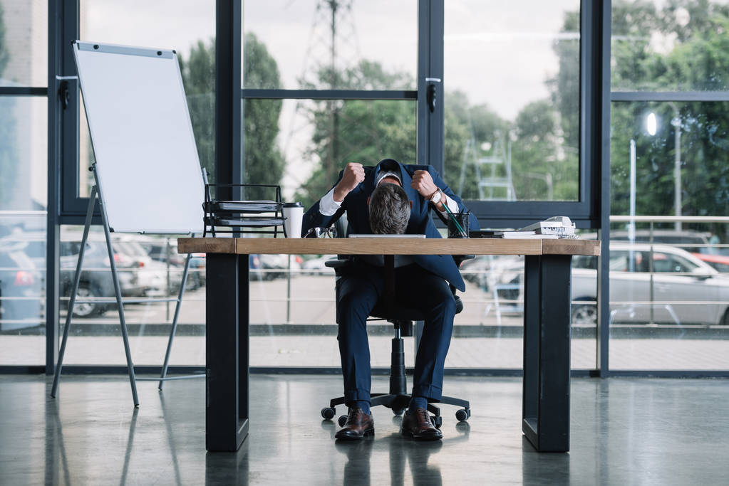 hombre de negocios sentado cerca de escritorio con las manos apretadas en la oficina moderna
  - Foto, Imagen
