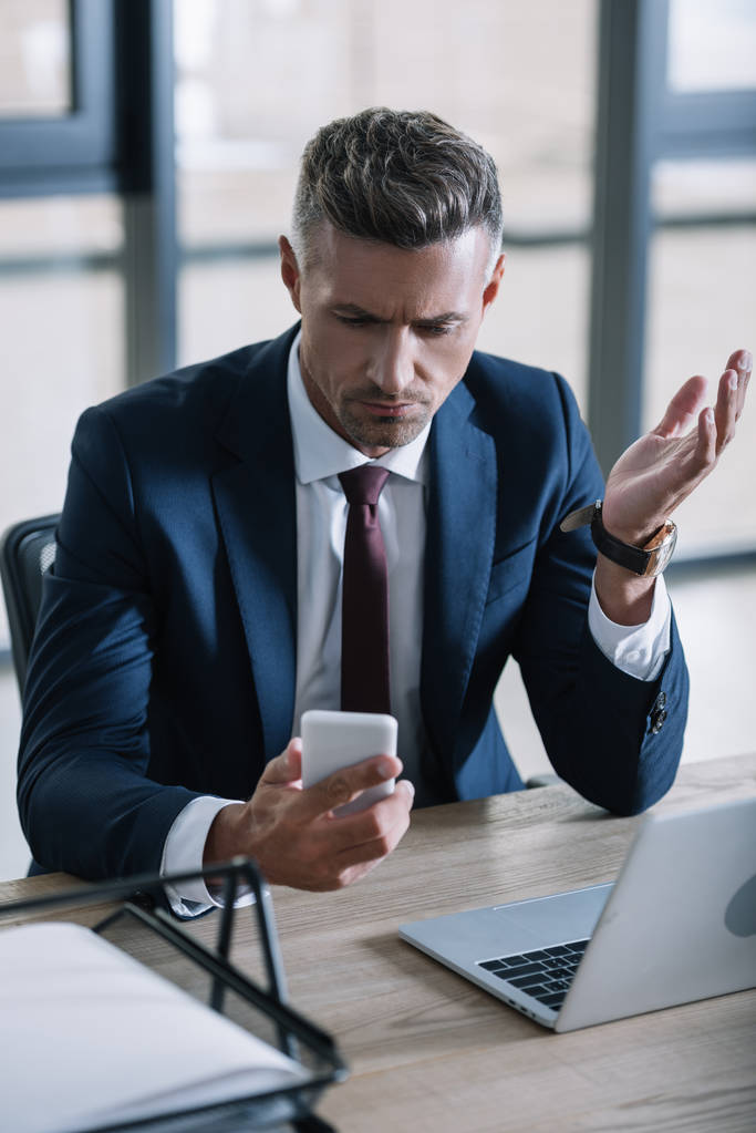 selektivní zaměření podnikatele na gestikulovat při pohledu na smartphone v kanceláři  - Fotografie, Obrázek