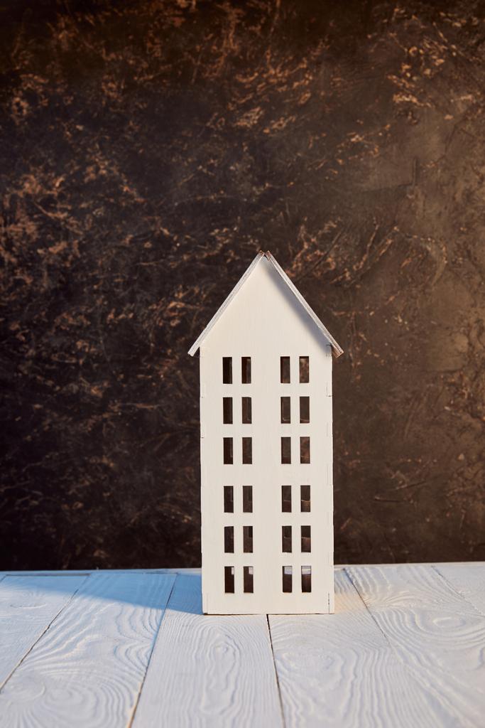 модель дома на белом деревянном столе возле коричневой текстурированной стены, концепция недвижимости
 - Фото, изображение