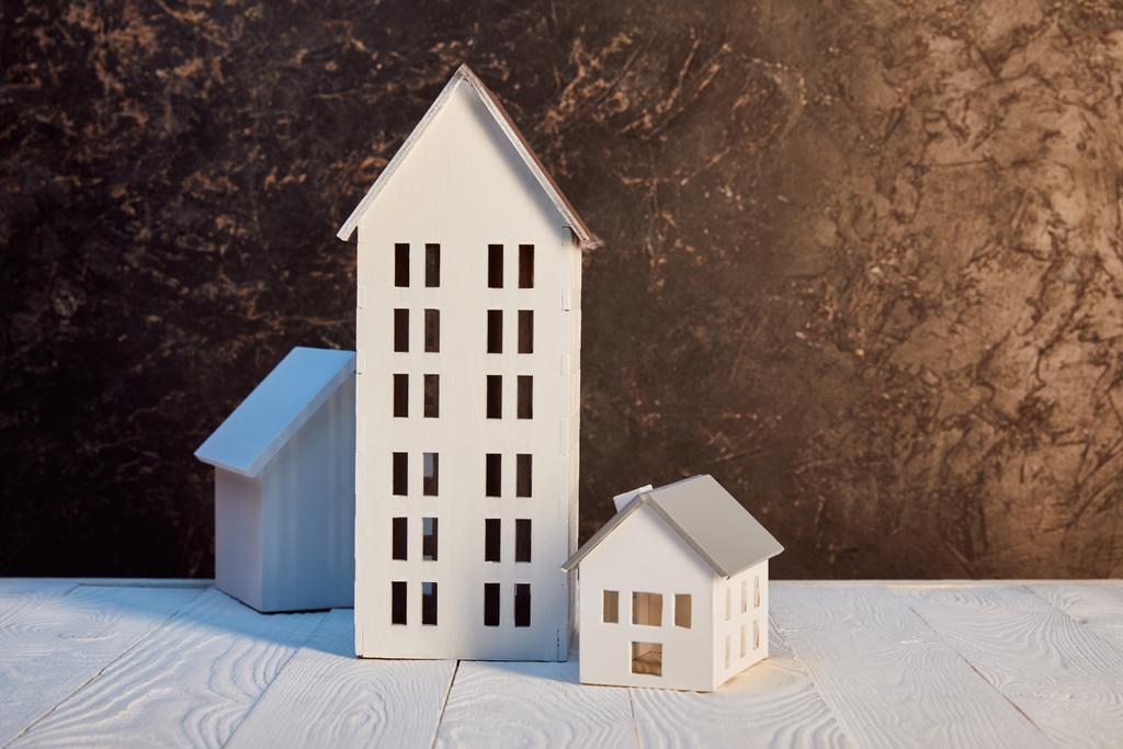 модели домов на белом деревянном столе возле коричневой текстурированной стены, концепция недвижимости
 - Фото, изображение