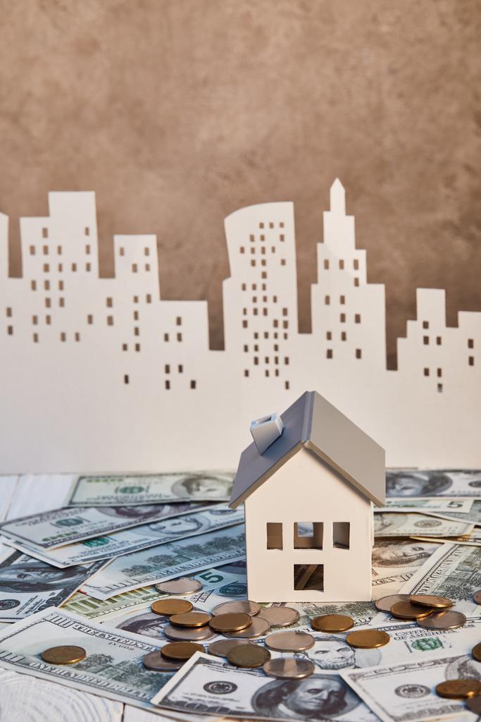 Model domu na banknotach dolara w pobliżu monet i miasto papieru na tle, koncepcja nieruchomości - Zdjęcie, obraz