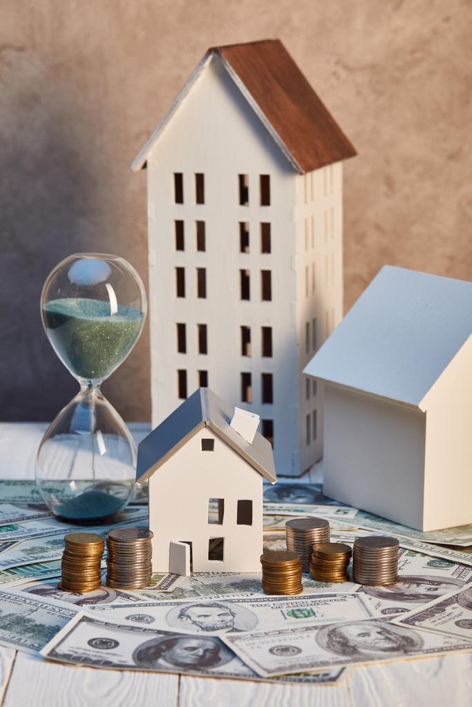 houses models and hourglass on dollar banknotes and coins, real estate concept - Photo, Image