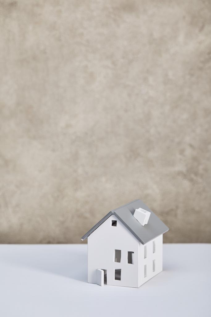 huis model op witte tafel in de buurt van Grey getextureerde muur, onroerend goed concept - Foto, afbeelding