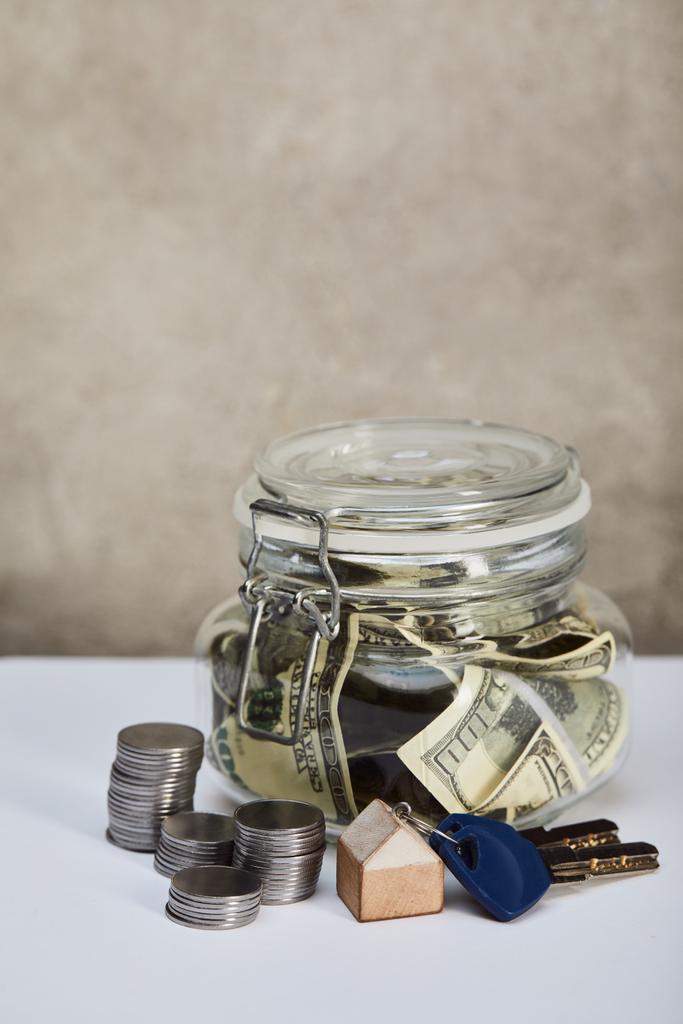 χρήμα με χαρτονομίσματα, κλειδιά και ασημένια κέρματα σε λευκό τραπέζι σε γκρίζο φόντο, έννοια ακινήτων - Φωτογραφία, εικόνα