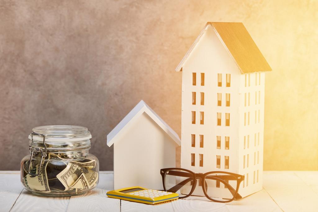 modelos das casas na tabela de madeira branca com óculos, calculadora e caixa de dinheiro na luz do sol, conceito real da propriedade
 - Foto, Imagem