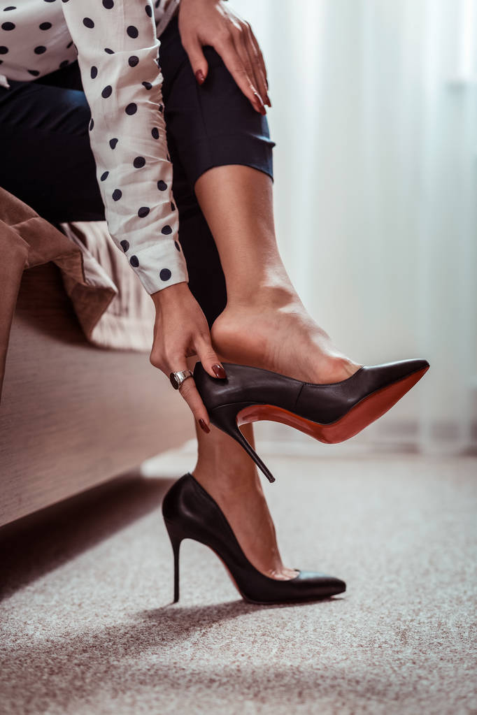 Уставшая привлекательная женщина снимает черные высокие каблуки после долгого рабочего дня
 - Фото, изображение