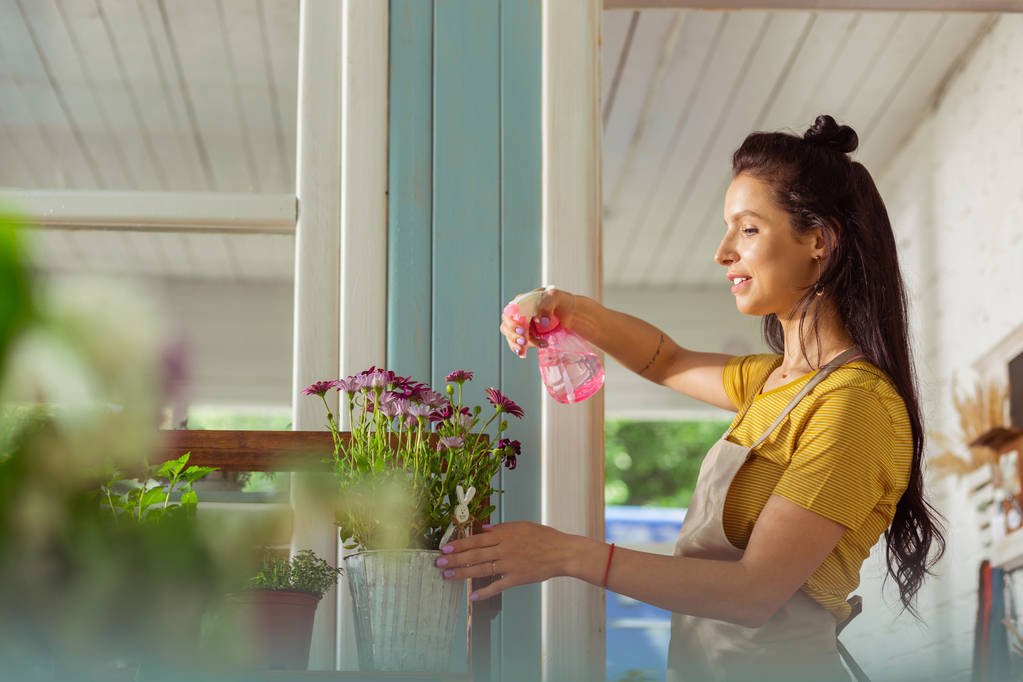 Συγκεντρωμένη γυναίκα που ψεκάζοντας φυτά έξω από το ανθοπωλείο της. - Φωτογραφία, εικόνα
