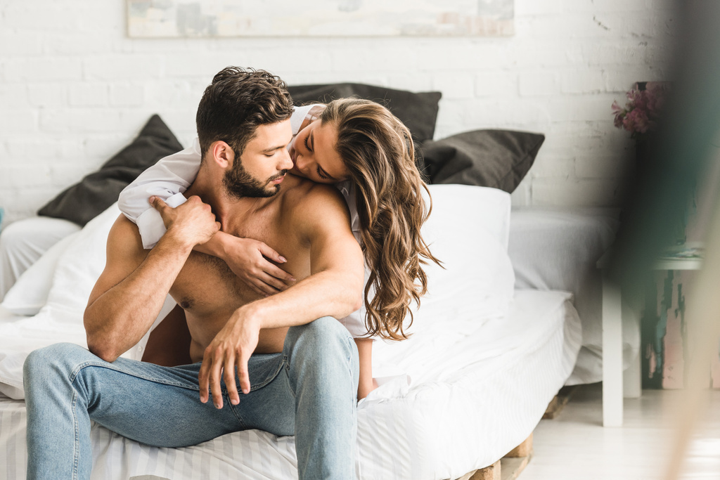 selectieve focus van twee mensen in liefde knuffelen terwijl ze in bed zitten - Foto, afbeelding