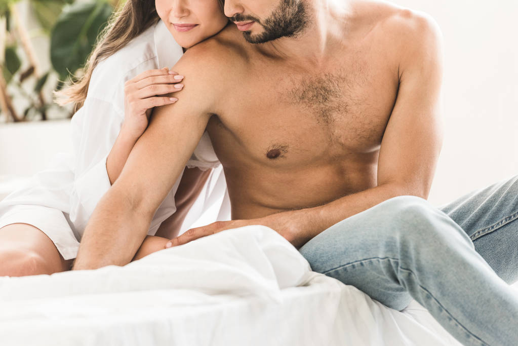 ostříhané zobrazení sexy páru sedícího v posteli a držení rukou - Fotografie, Obrázek