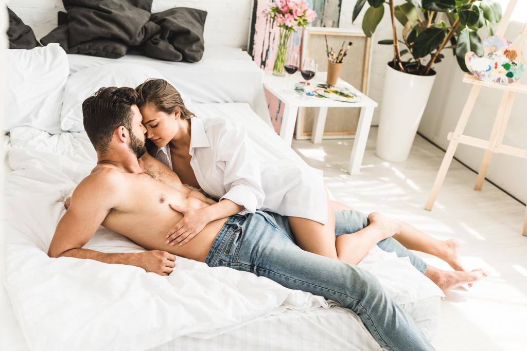 女の子が男の胴に触れている間にベッドに横たわっているセクシーな若いカップルの完全な長さのビュー - 写真・画像