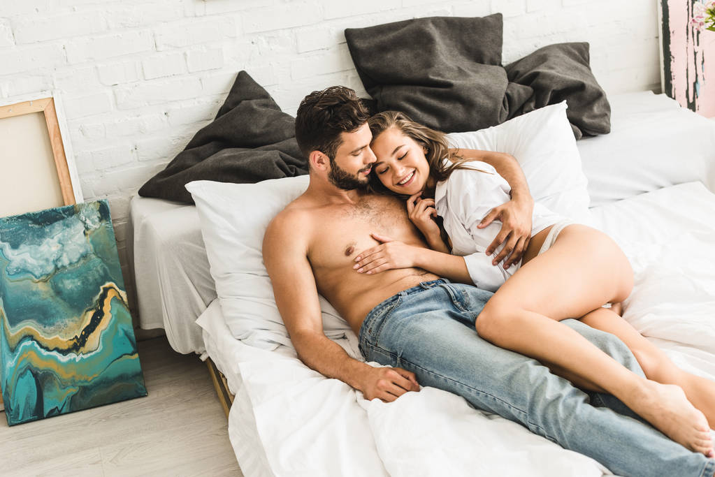 szexi pár feküdt az ágyban, és mosolyogva, miközben lány megható félmeztelen ember - Fotó, kép