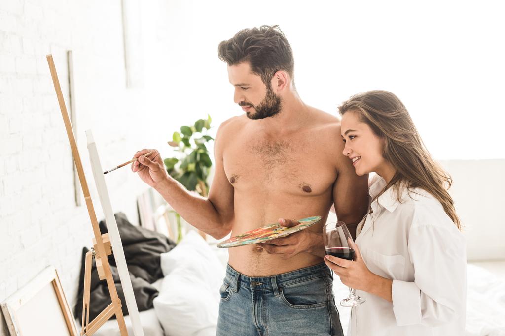 sexy young man drawing while girl standing with wine and looking at painting - Photo, Image