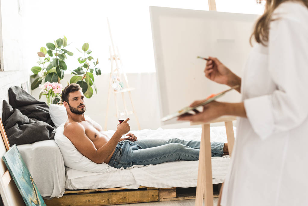 selectieve focus van de mens liggend in bed met wijn en meisje tekenen met borstel - Foto, afbeelding