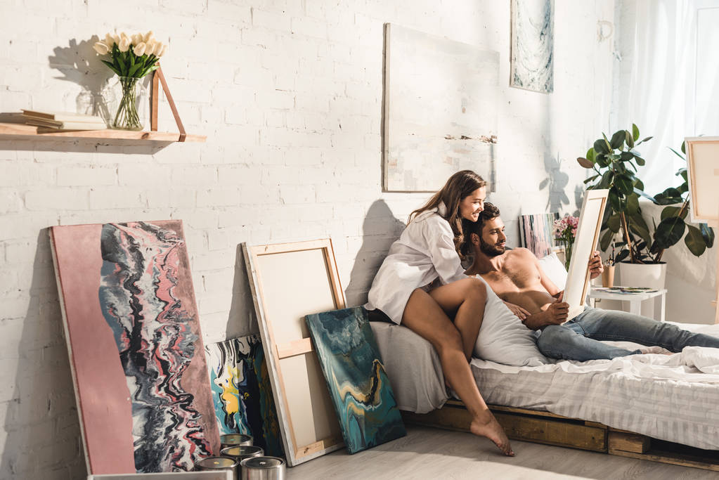 šťastný mladý pár sedí v posteli a dívá se na malování  - Fotografie, Obrázek