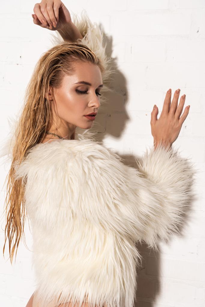 σέξι κορίτσι με βρεγμένα μαλλιά σε λευκό ψεύτικη γούνα παλτό σε λευκό φόντο - Φωτογραφία, εικόνα