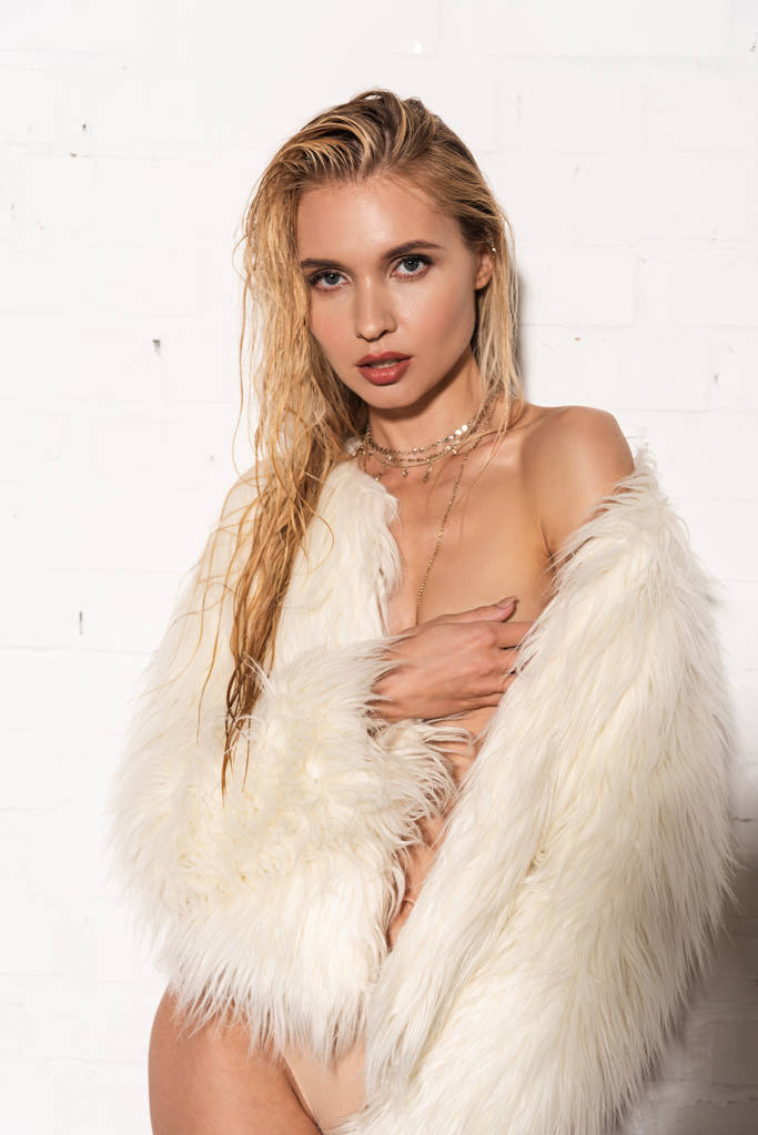 白い背景に胸に触れる白い偽の毛皮のコートで濡れた髪を持つセクシーな裸の若い女性 - 写真・画像