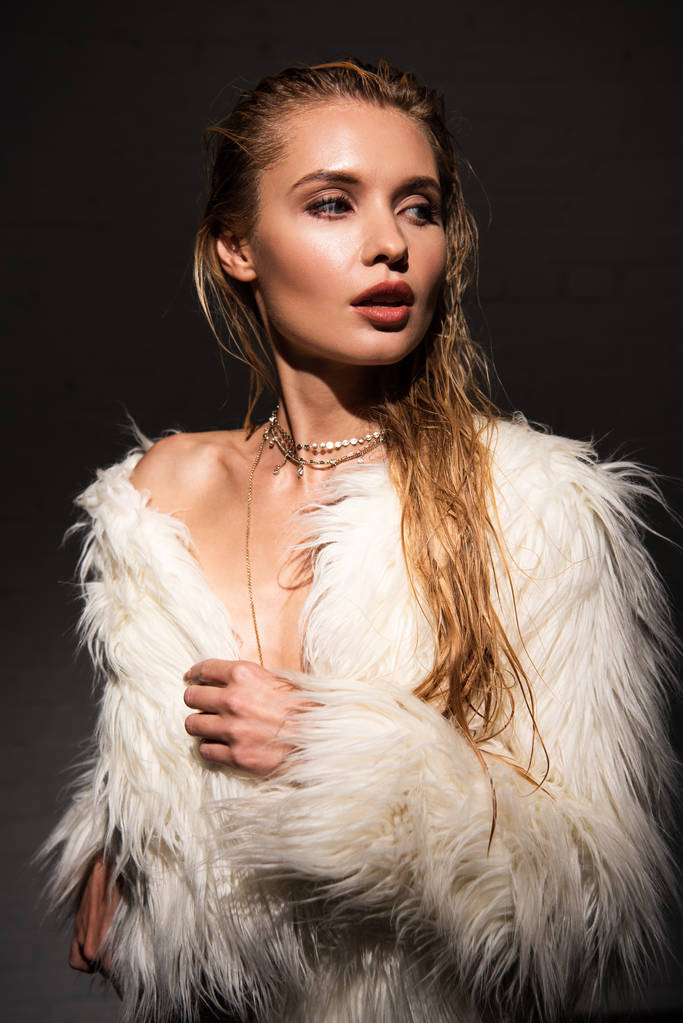 sexy naked young woman with wet blonde hair in white faux fur coat looking away isolated on black - Photo, Image