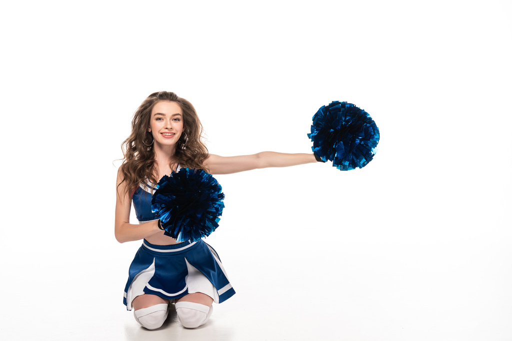 szczęśliwy cheerleaderka dziewczyna w niebieskim mundurze siedzi z pompony na podłodze na białym tle - Zdjęcie, obraz