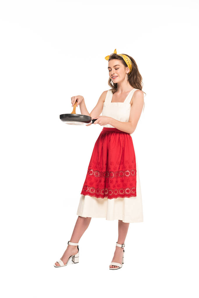 vista completa de la joven ama de casa en vestido y delantal con espátula de madera y sartén aislados en blanco
 - Foto, imagen