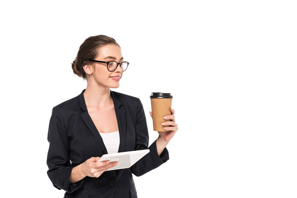 jovem sorridente empresária bem sucedida em terno preto e óculos segurando café para ir e tablet digital isolado em branco
 - Foto, Imagem