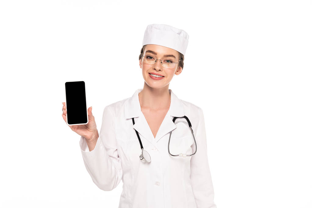 nuori onnellinen lääkäri valkoisessa takissa stetoskooppi osoittaa älypuhelin tyhjä näyttö eristetty valkoinen
 - Valokuva, kuva