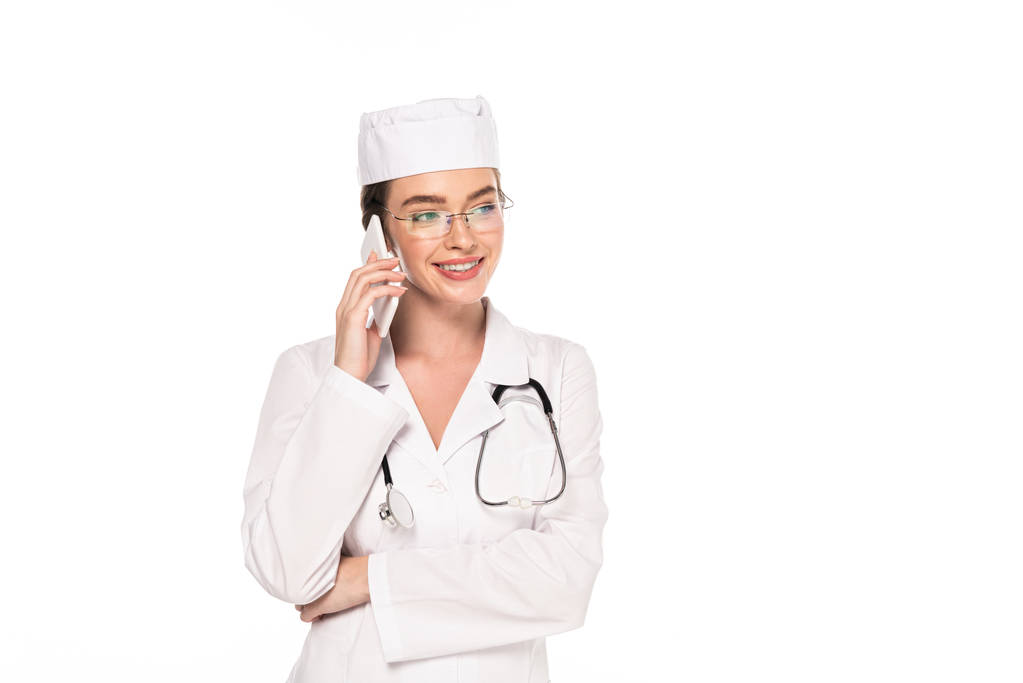 молодой счастливый доктор в белом халате со стетоскопом разговаривает на смартфоне изолирован на белом
 - Фото, изображение