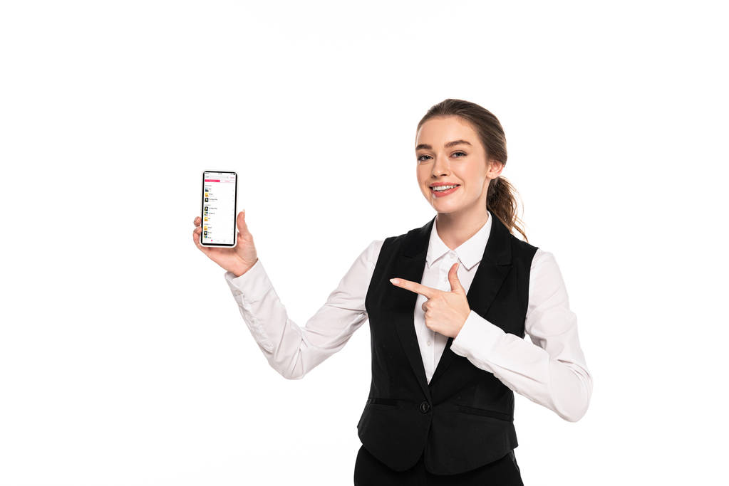 キエフ、ウクライナ - 2019年4月7日:白で隔離されたスマートフォン上のアップルの音楽アプリで指を指差す幸せな若いウェイトレス - 写真・画像