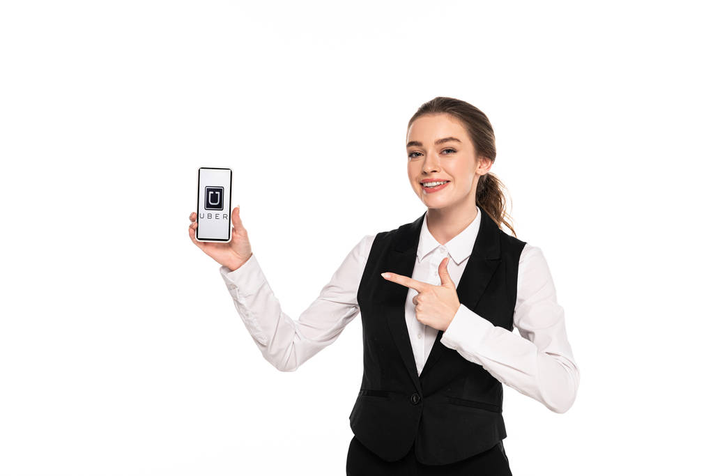 KYIV, UKRAINE - APRIL 7, 2019: happy young waitress pointing with finger at uber app on smartphone isolated on white - Photo, Image