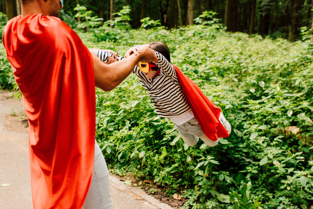padre en capa de superhéroe rojo girando alrededor de hijo pequeño
  - Foto, imagen