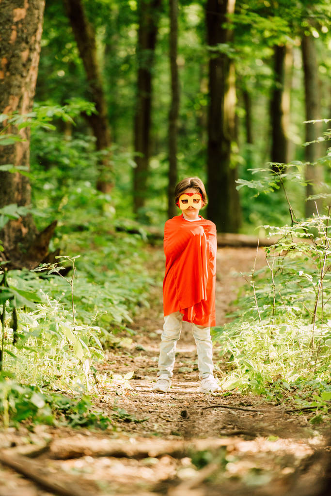 pełny widok długości małego chłopca w kostiumie superbohatera stojącego w lesie  - Zdjęcie, obraz