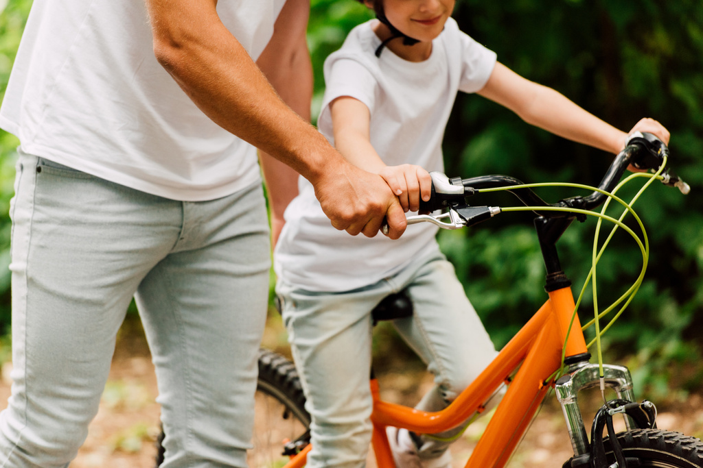 vista recortada de hijo montar en bicicleta y padre sosteniendo asas para ayudar a niño a montar
 - Foto, imagen