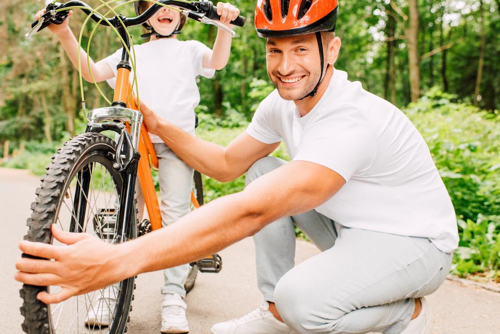 vista recortada del hijo de pie y sosteniendo asas de bicicleta mientras el padre revisa la rueda
  - Foto, Imagen