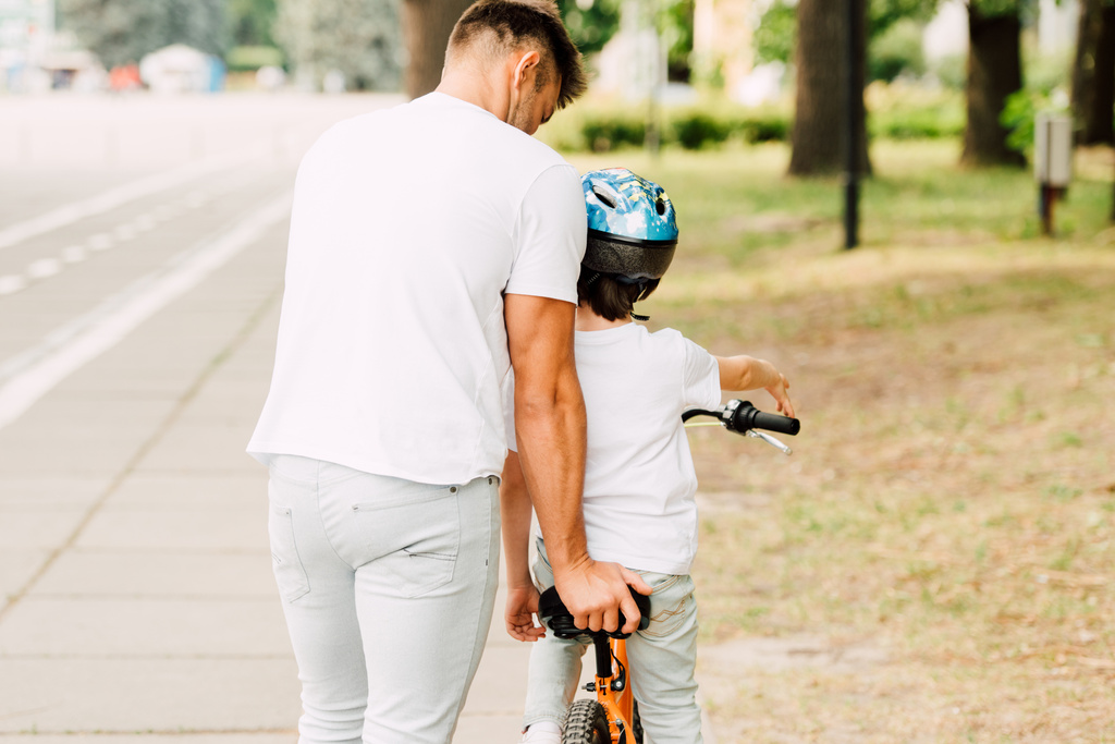 вид ззаду батька, який допомагає синові їздити на велосипеді, коли дитина сидить на велосипеді
 - Фото, зображення