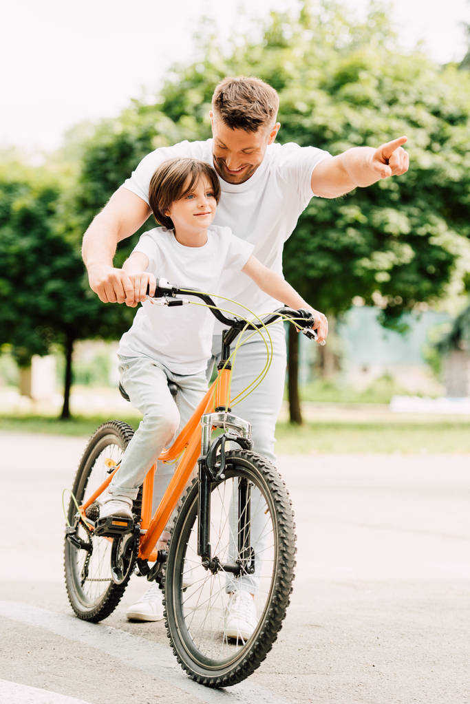 pohled plný délky syna jízdy na kole zatímco otec ukazoval prstem - Fotografie, Obrázek