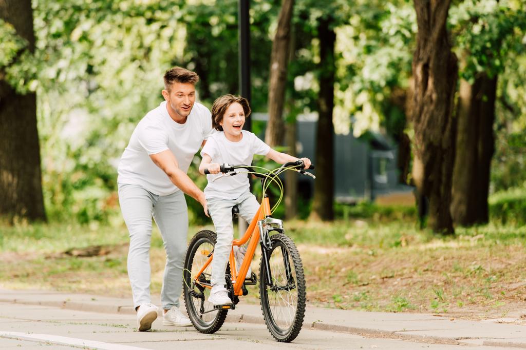 повнометражний вид батька штовхає велосипед, а син кричить на велосипеді
 - Фото, зображення