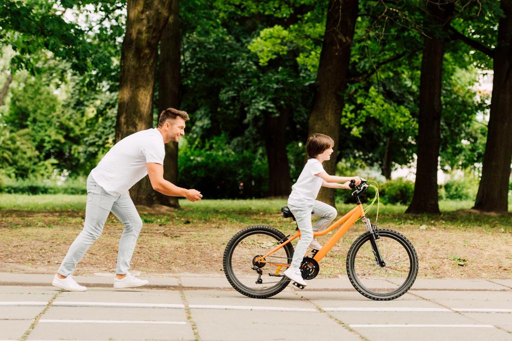 vista lateral del padre vitoreando hijo mientras niño montar en bicicleta
 - Foto, imagen