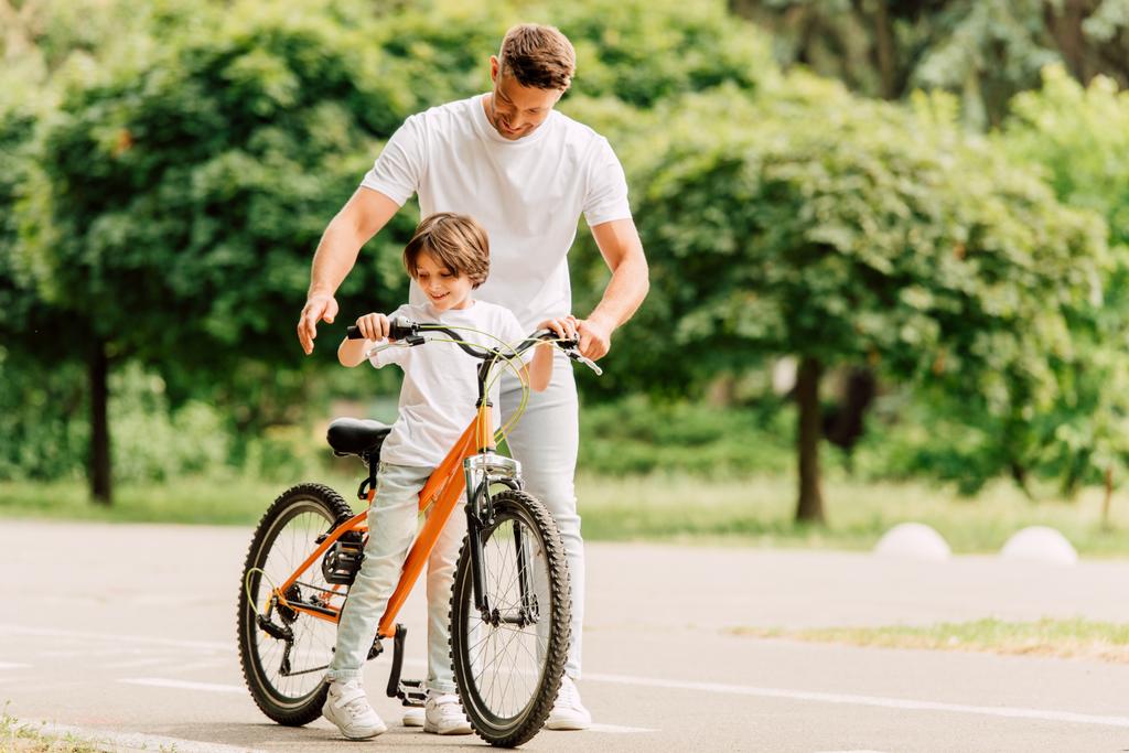 vista completa de la longitud de padre e hijo mirando en bicicleta mientras está de pie en la carretera
 - Foto, Imagen