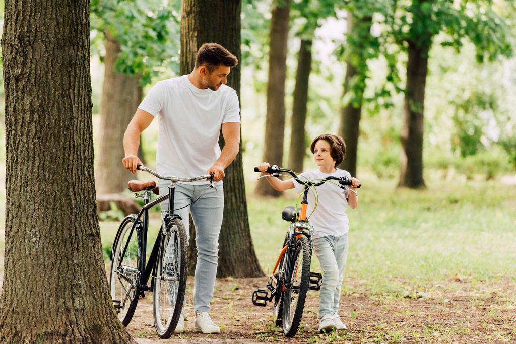 pełny widok długości ojca i syna z rowerami pieszo w parku i patrząc na siebie - Zdjęcie, obraz