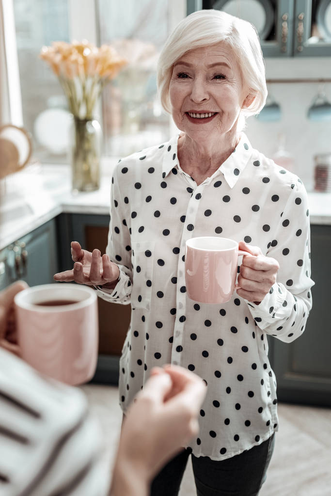 Donna anziana alla moda che sorride e sembra felice mentre beve il tè
 - Foto, immagini