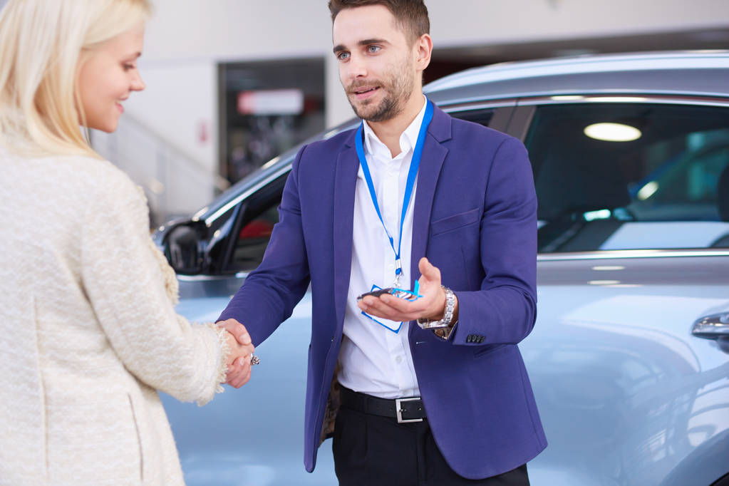 Πωλητής αυτοκινήτων πωλεί ένα αυτοκίνητο σε χαρούμενο πελάτη στην αντιπροσωπεία αυτοκινήτων και τα χέρια πάνω από τα κλειδιά. - Φωτογραφία, εικόνα