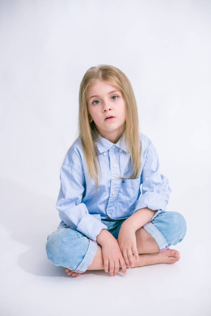 Красива модна маленька дівчинка з світлим волоссям в джинсовому одязі на білому тлі в студії
 - Фото, зображення